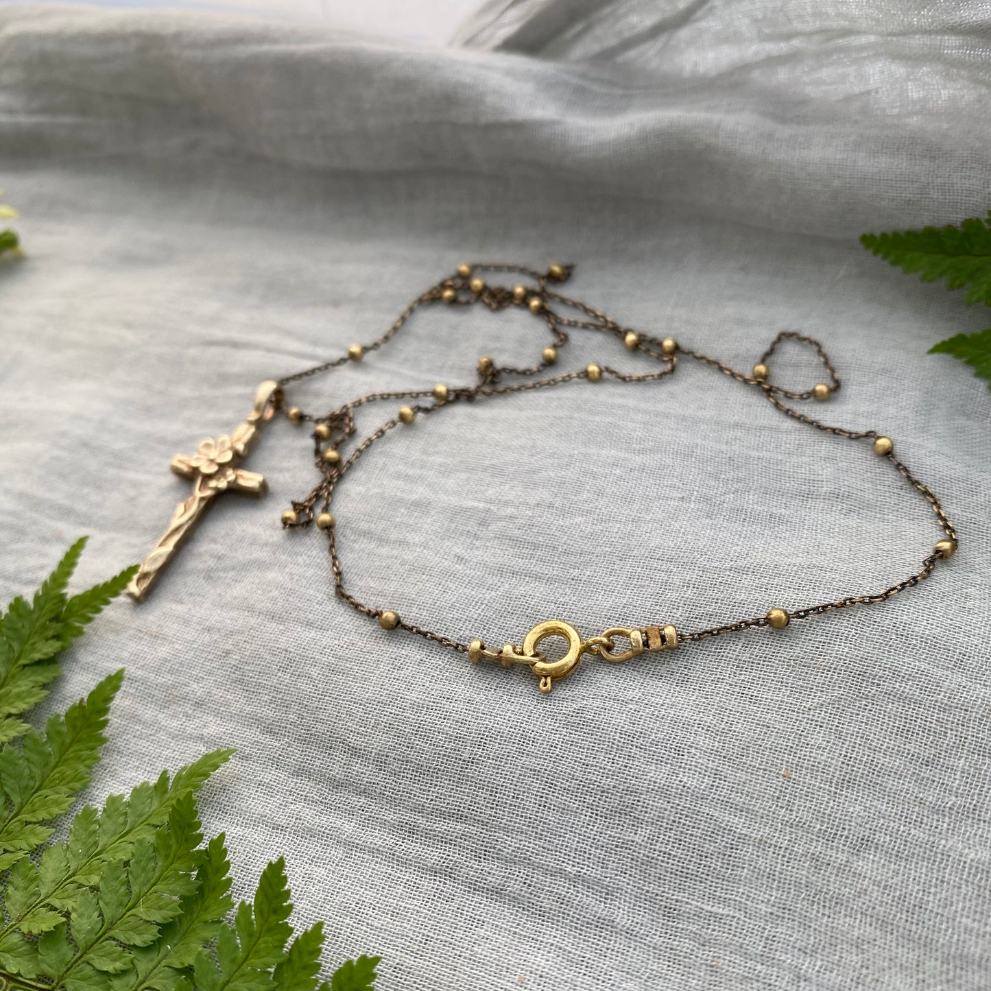Dainty antiqued brass cross necklace with forget-me-not blossoms and leaves and wood grain texture on antiqued brass satellite cable chain