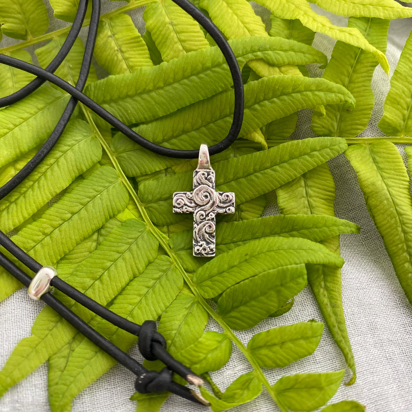 chunky small sterling silver cross on black leather cord with unique swirling wave design, gift for men and women, handcarved and produced in USA