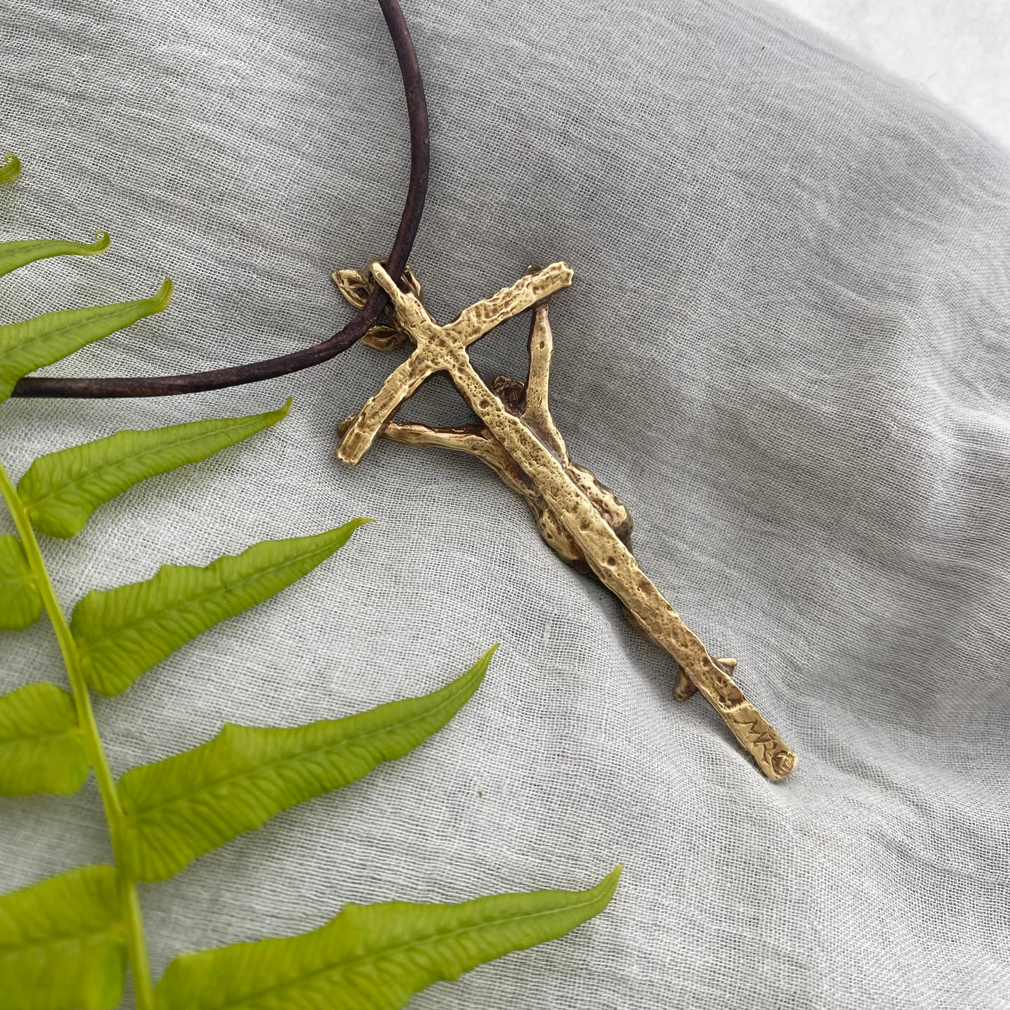 Large brass crucifix necklace; brown leather cord; realistic hand carved corpus; Jesus' suffering, death; leaves symbolizing new life