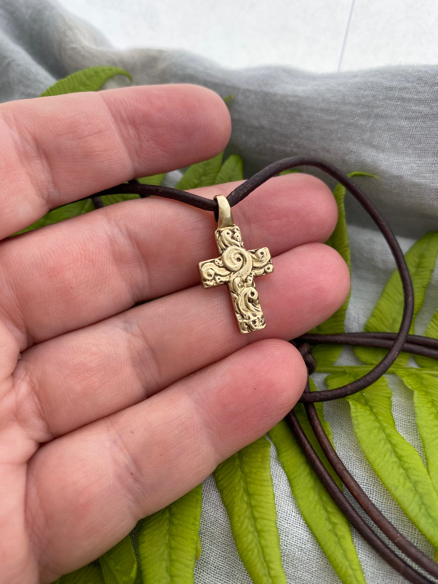 chunky small brass cross on brown leather cord with unique swirling wave design, gift for men and women, hand carved and produced in USA