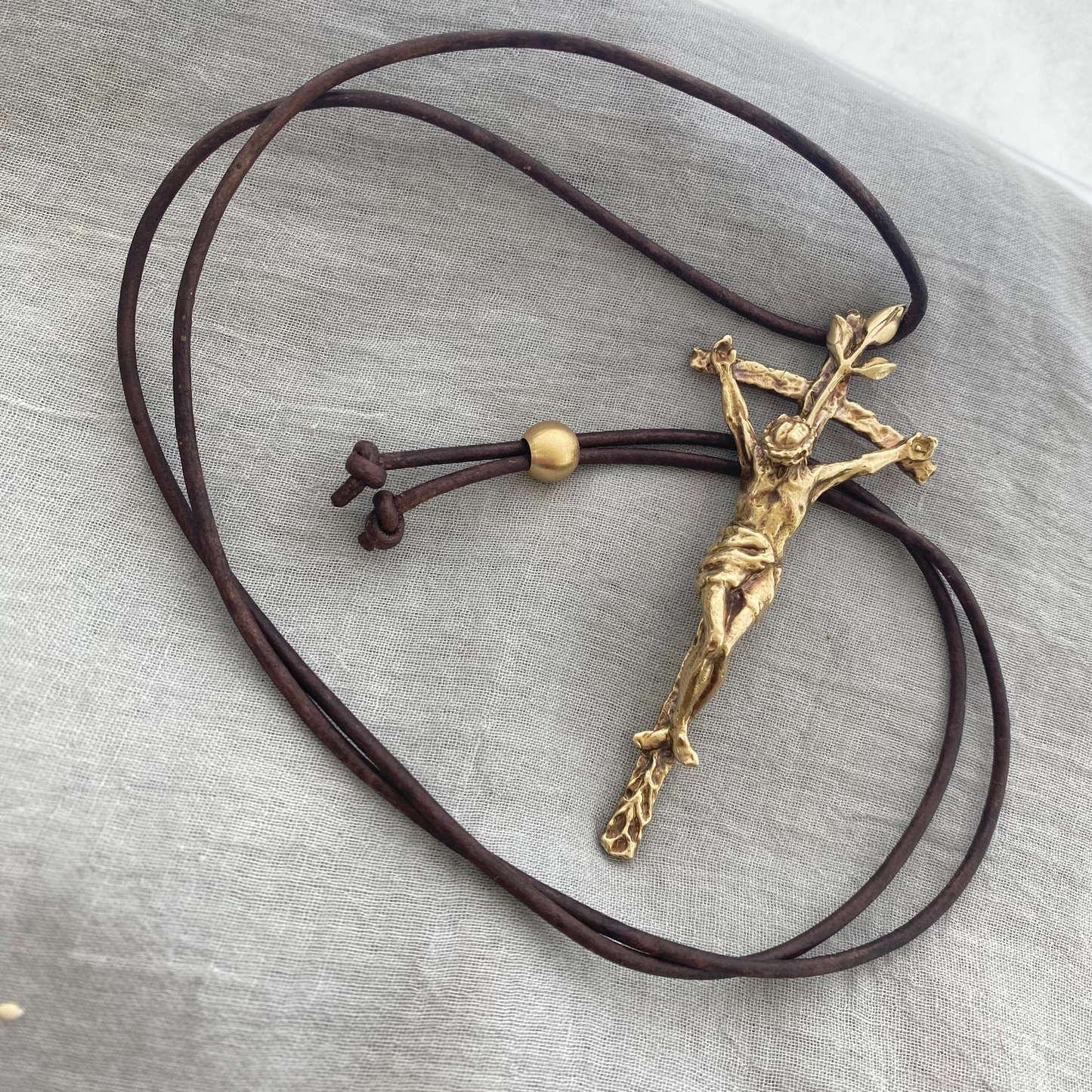 Large brass crucifix necklace; brown leather cord; realistic hand carved corpus; Jesus' suffering, death; leaves symbolizing new life