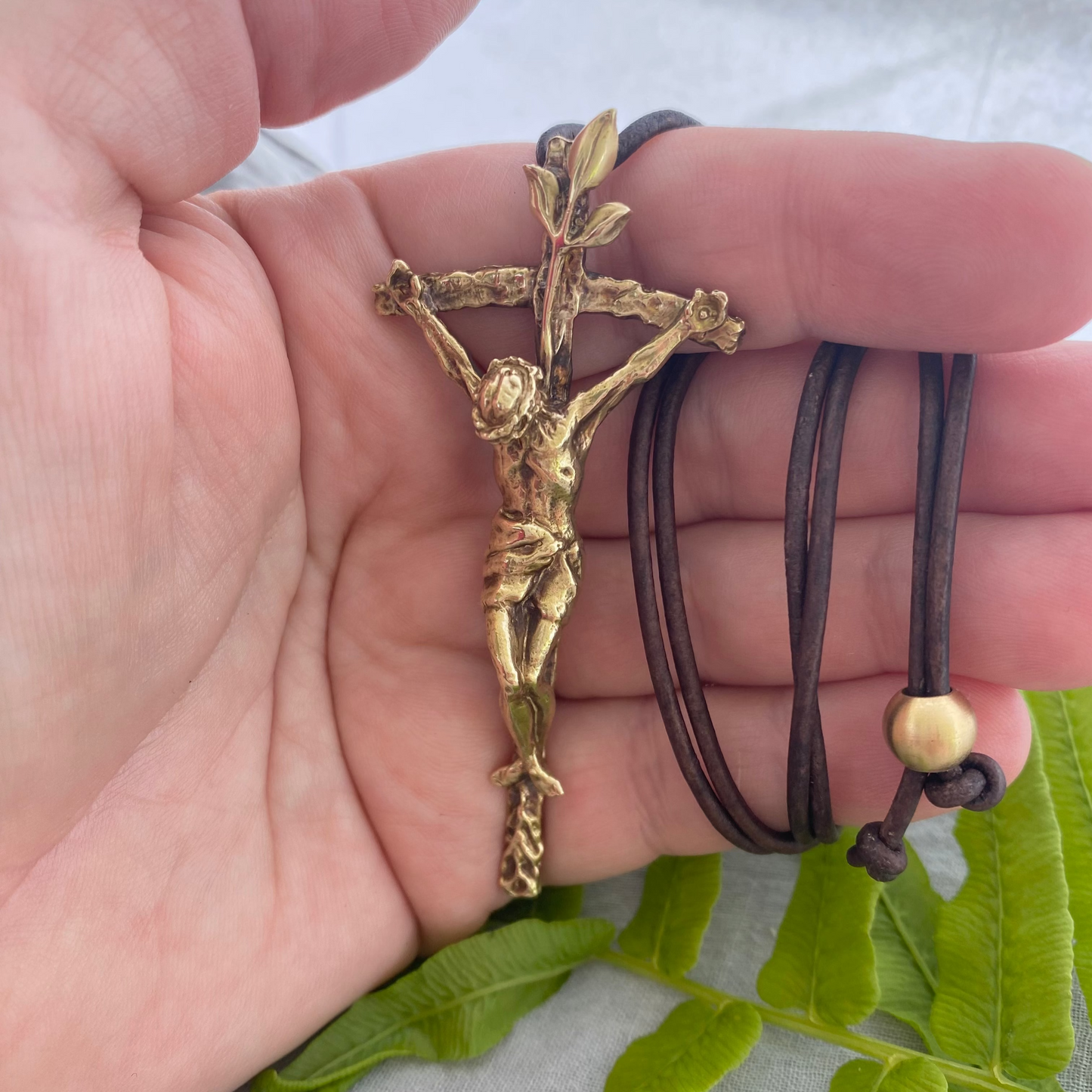 Large brass crucifix necklace; brown leather cord; realistic hand carved corpus; Jesus' suffering, death; leaves symbolizing new life