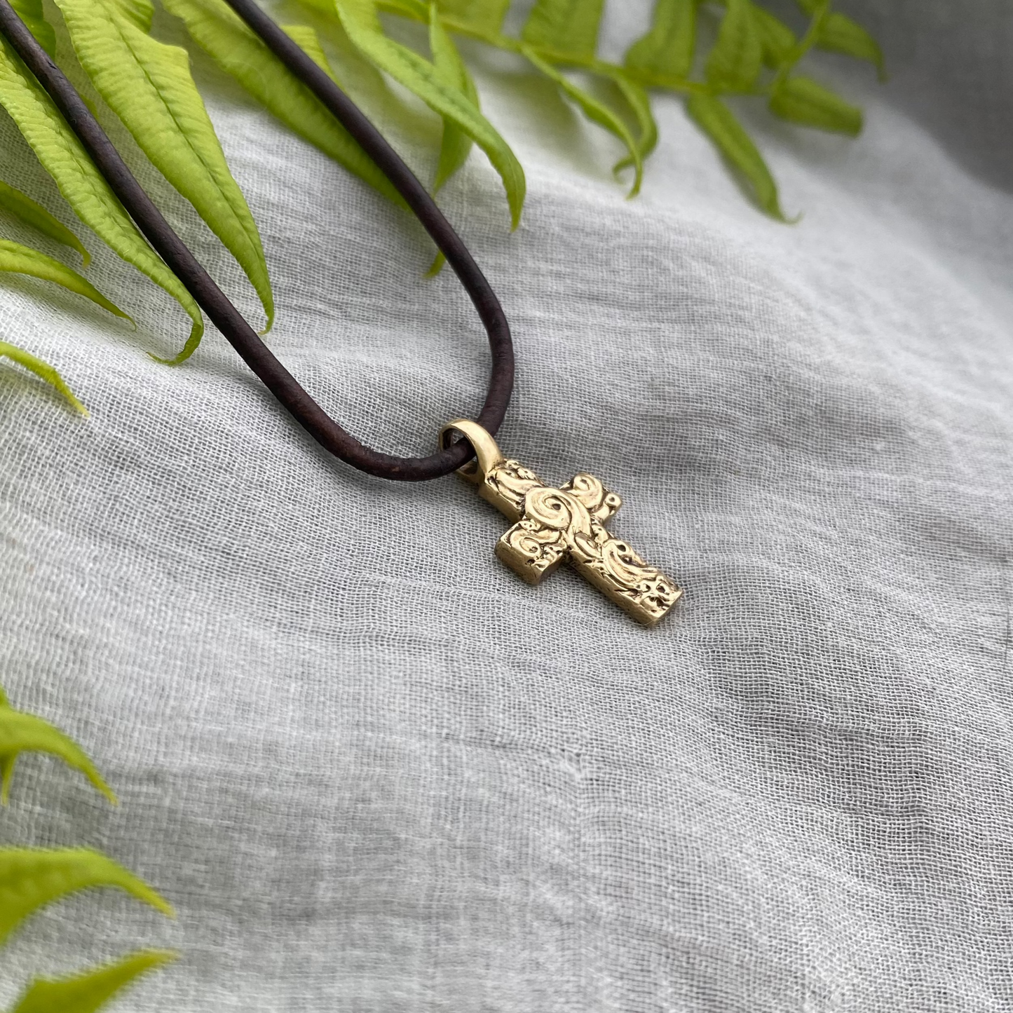 chunky small brass cross on brown leather cord with unique swirling wave design, gift for men and women, hand carved and produced in USA