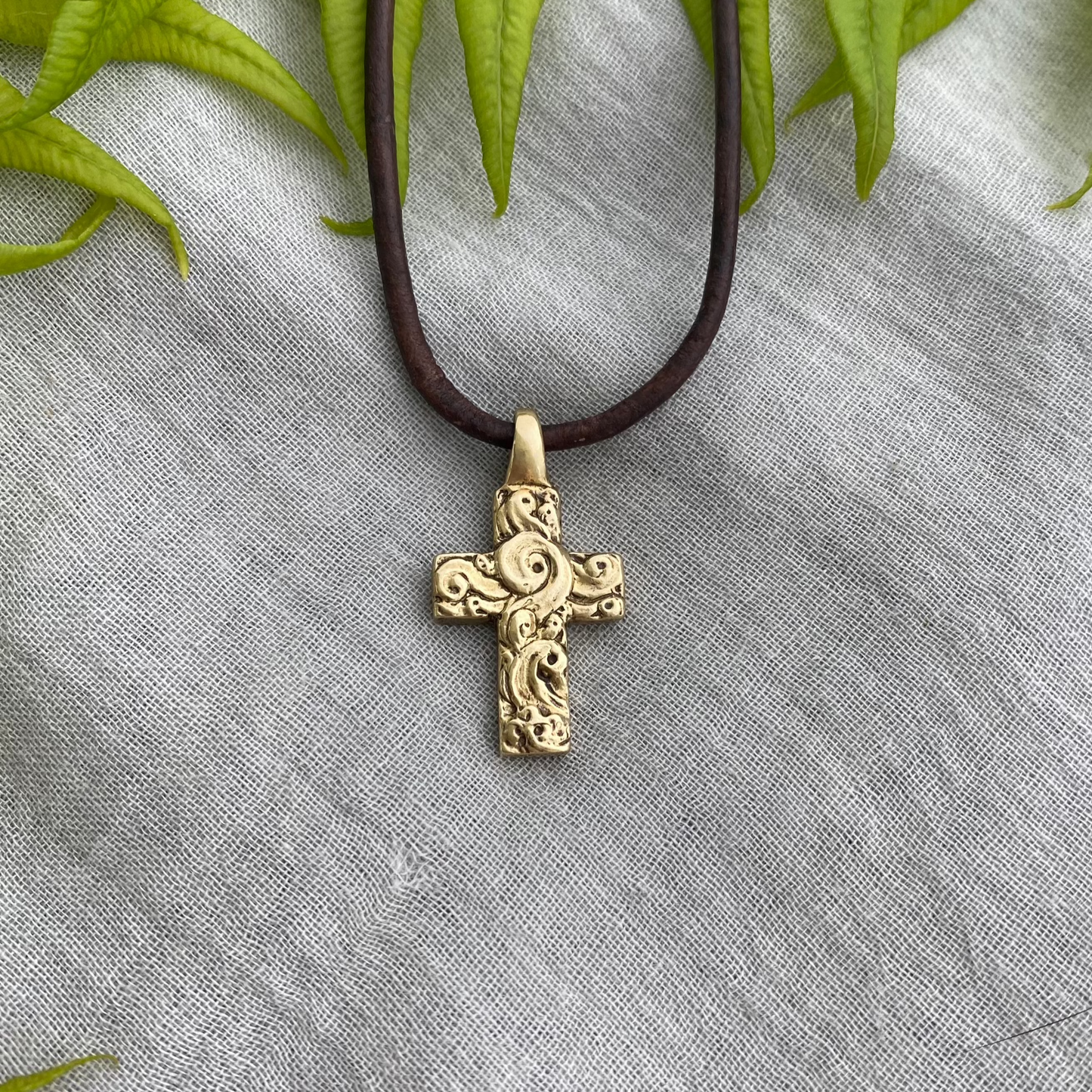 chunky small brass cross on brown leather cord with unique swirling wave design, gift for men and women, hand carved and produced in USA