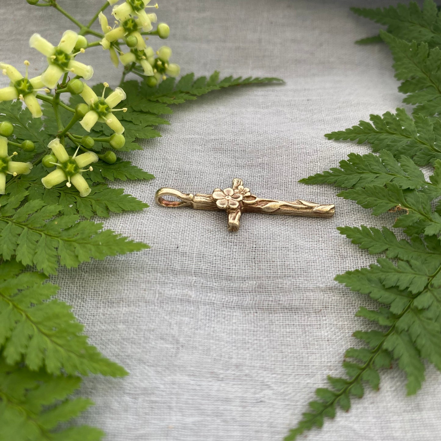 Dainty floral cross pendant for a necklace; gold toned brass; forget-me-not blossoms, leaves, wood grain texture; feminine flower; no chain