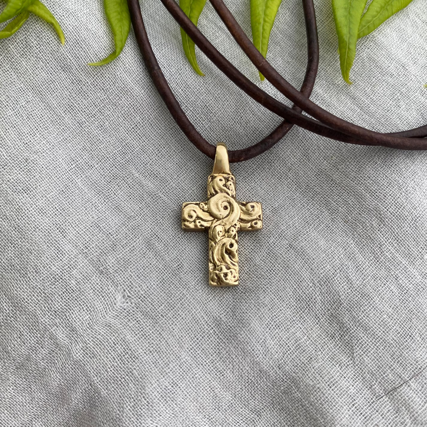 chunky small brass cross on brown leather cord with unique swirling wave design, gift for men and women, hand carved and produced in USA
