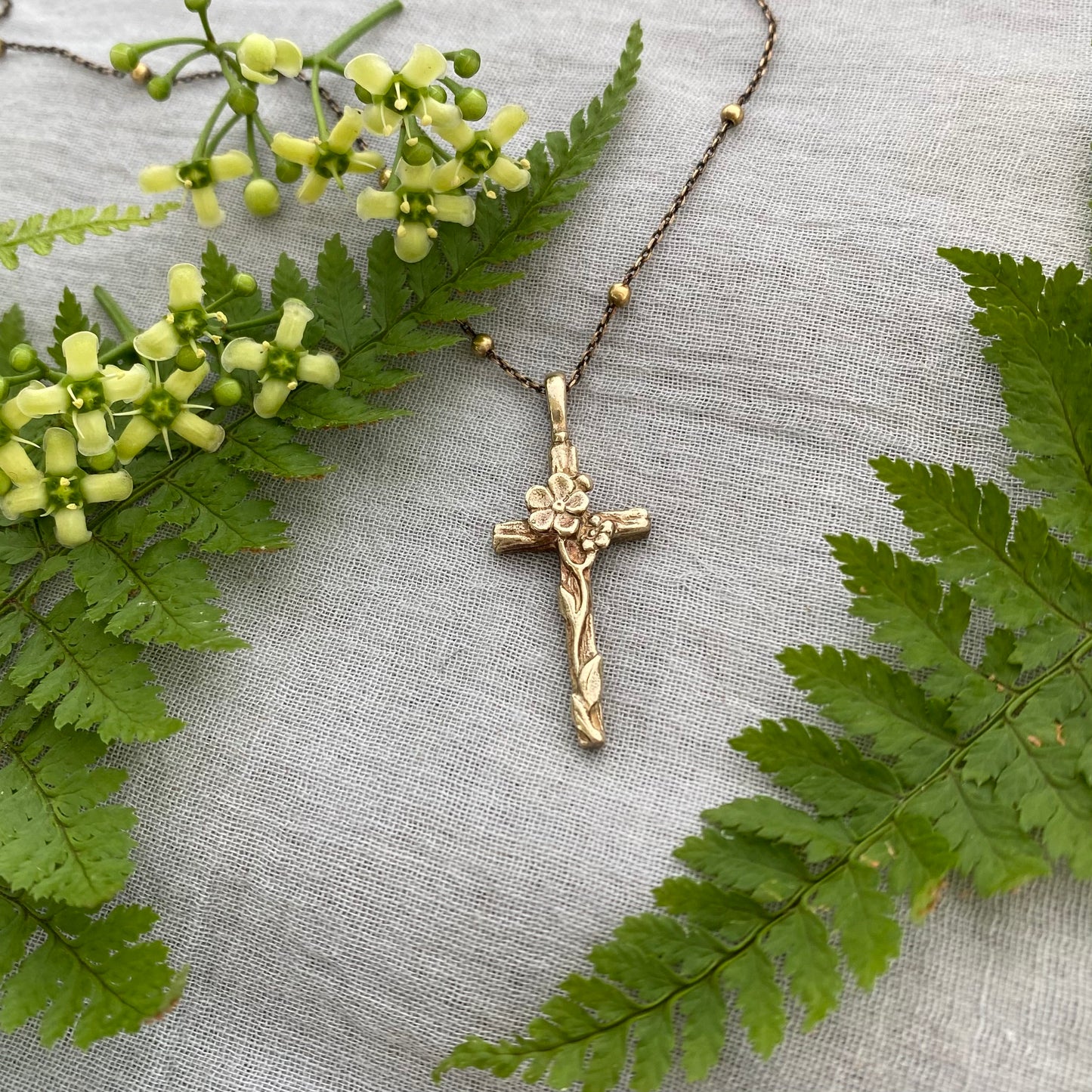 Dainty antiqued brass cross necklace with forget-me-not blossoms and leaves and wood grain texture on antiqued brass satellite cable chain