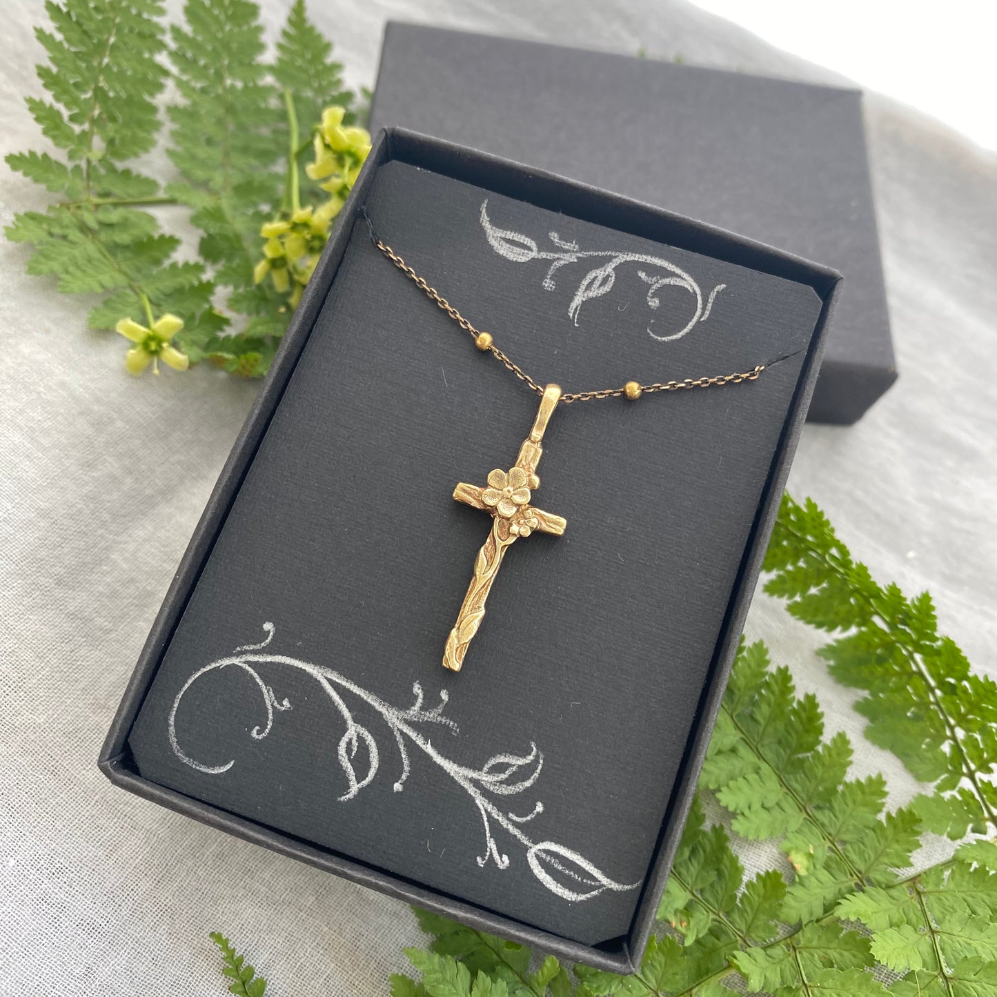Dainty antiqued brass cross necklace with forget-me-not blossoms and leaves and wood grain texture on antiqued brass satellite cable chain