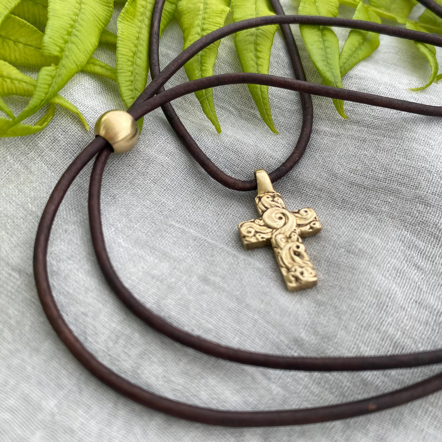 chunky small brass cross on brown leather cord with unique swirling wave design, gift for men and women, hand carved and produced in USA