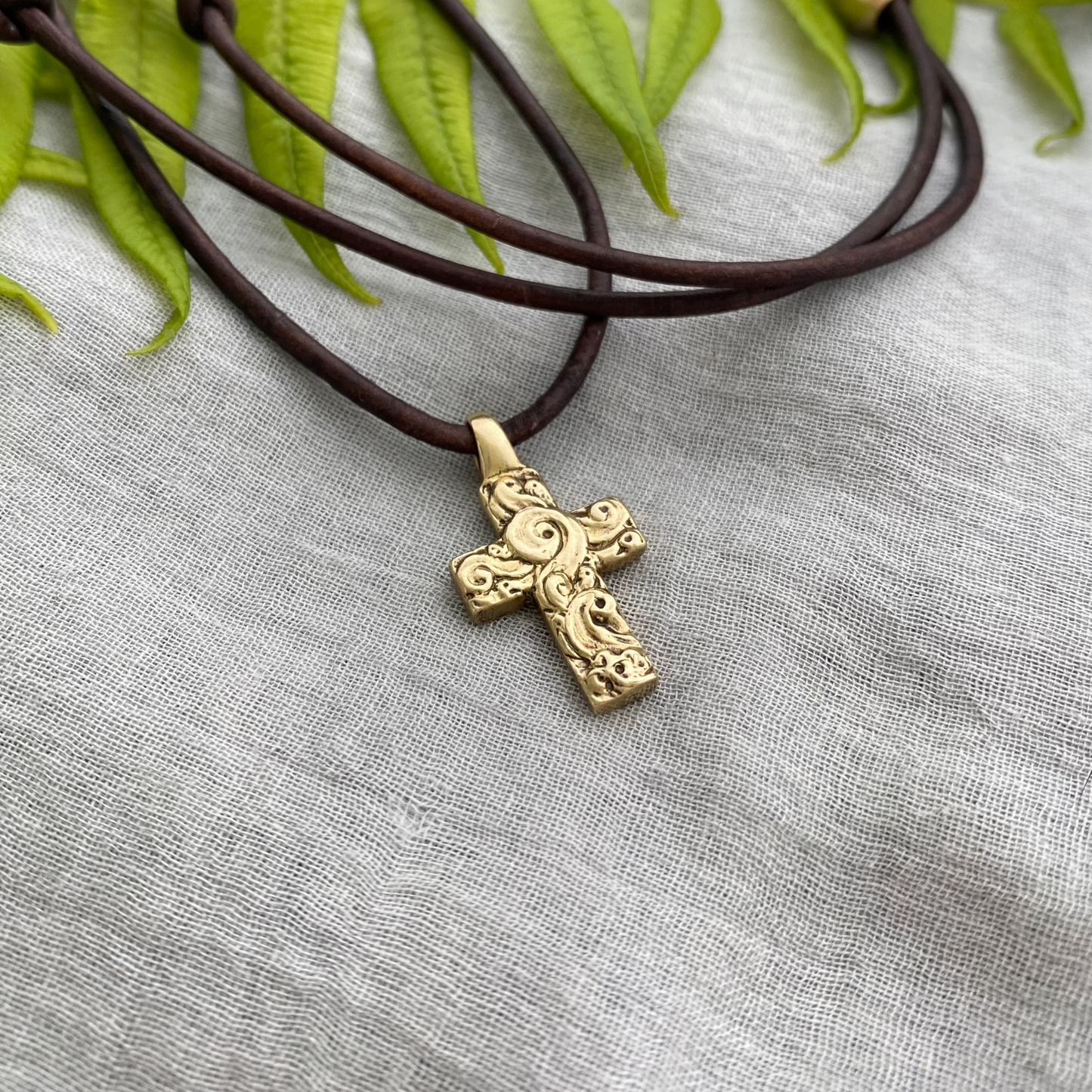 chunky small brass cross on brown leather cord with unique swirling wave design, gift for men and women, hand carved and produced in USA