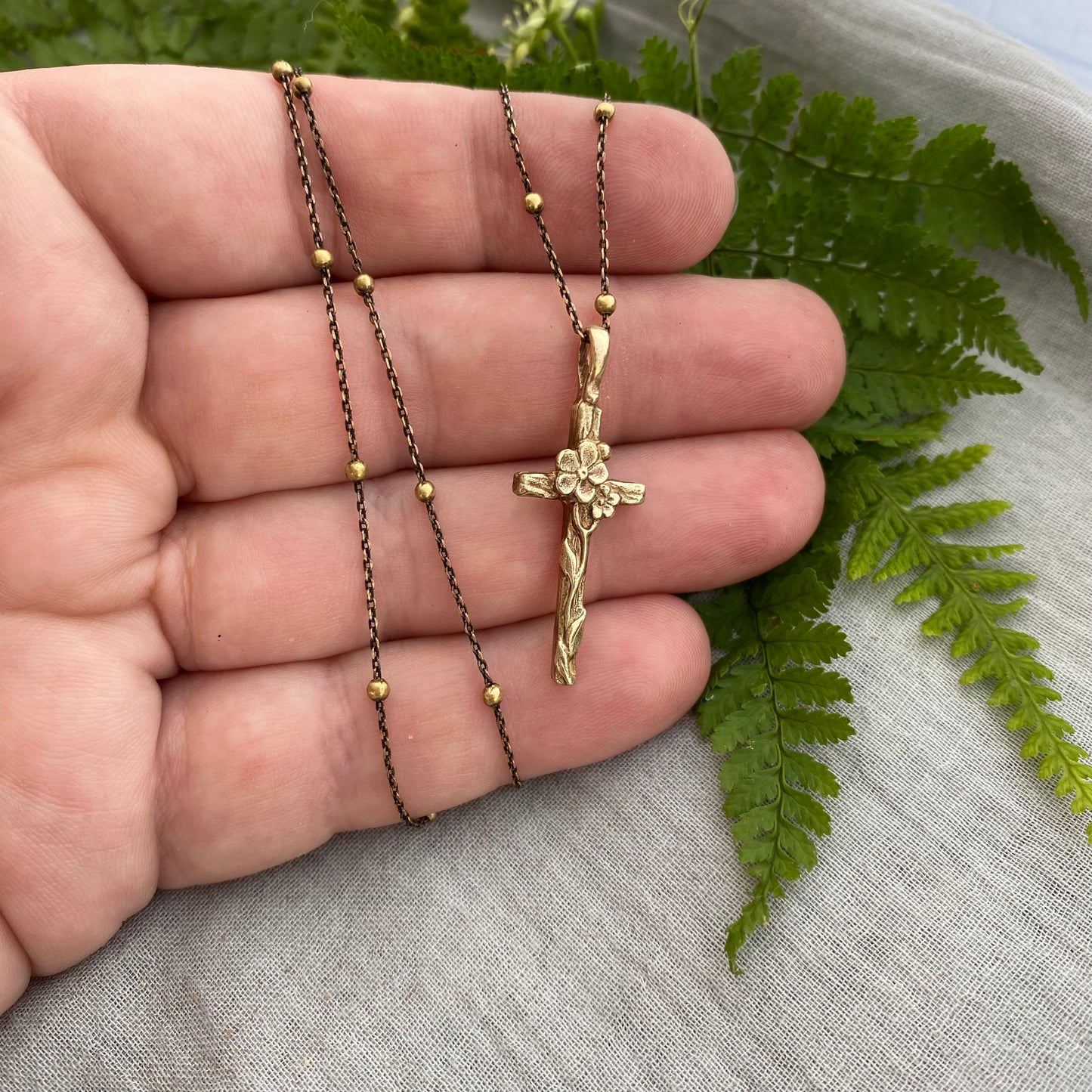 Dainty antiqued brass cross necklace with forget-me-not blossoms and leaves and wood grain texture on antiqued brass satellite cable chain