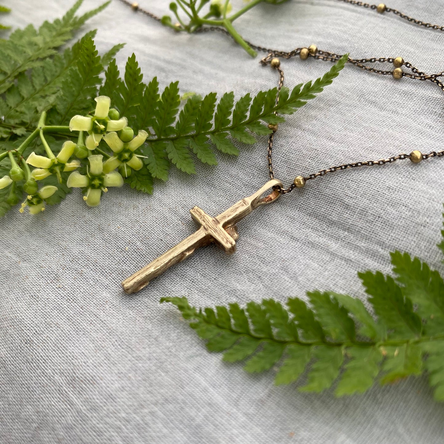 Dainty antiqued brass cross necklace with forget-me-not blossoms and leaves and wood grain texture on antiqued brass satellite cable chain