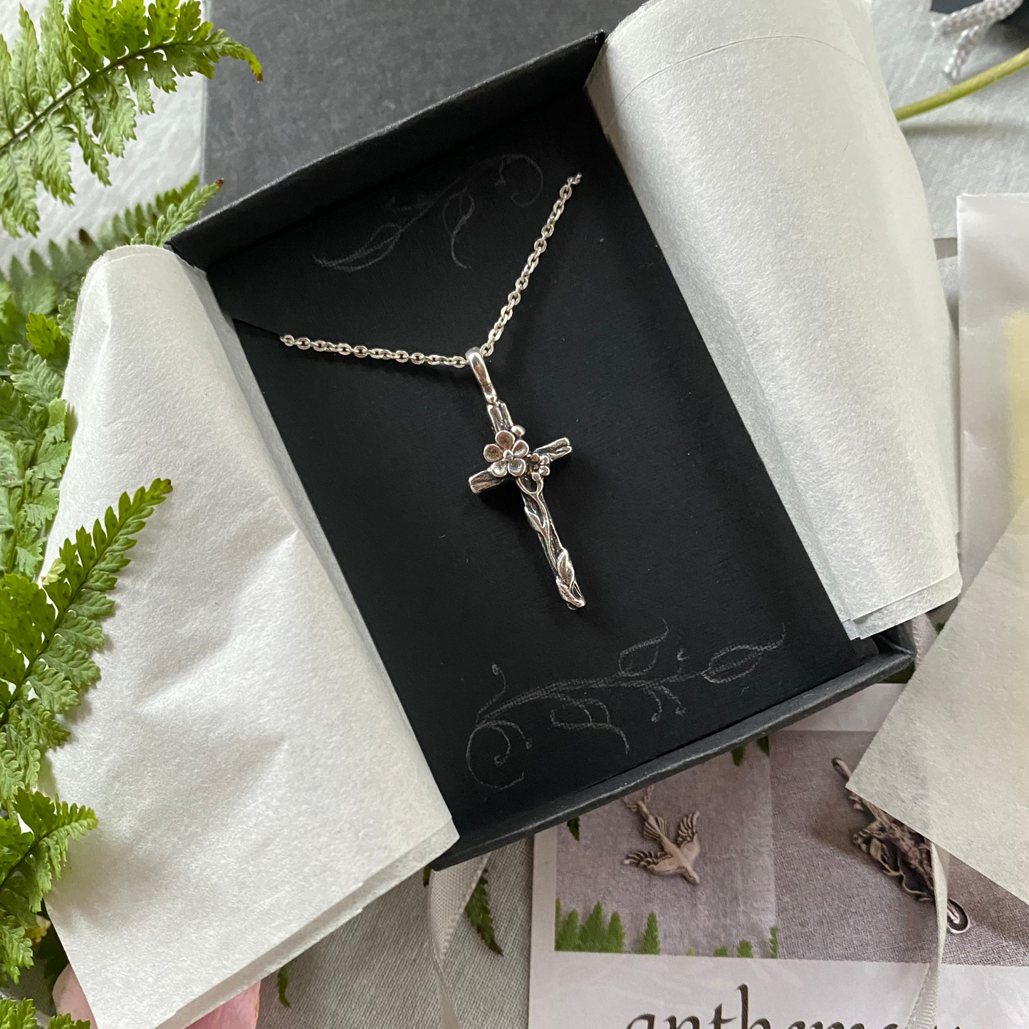 Dainty silver cross necklace with graceful forget-me-not blossoms and leaves and woodgrain texture