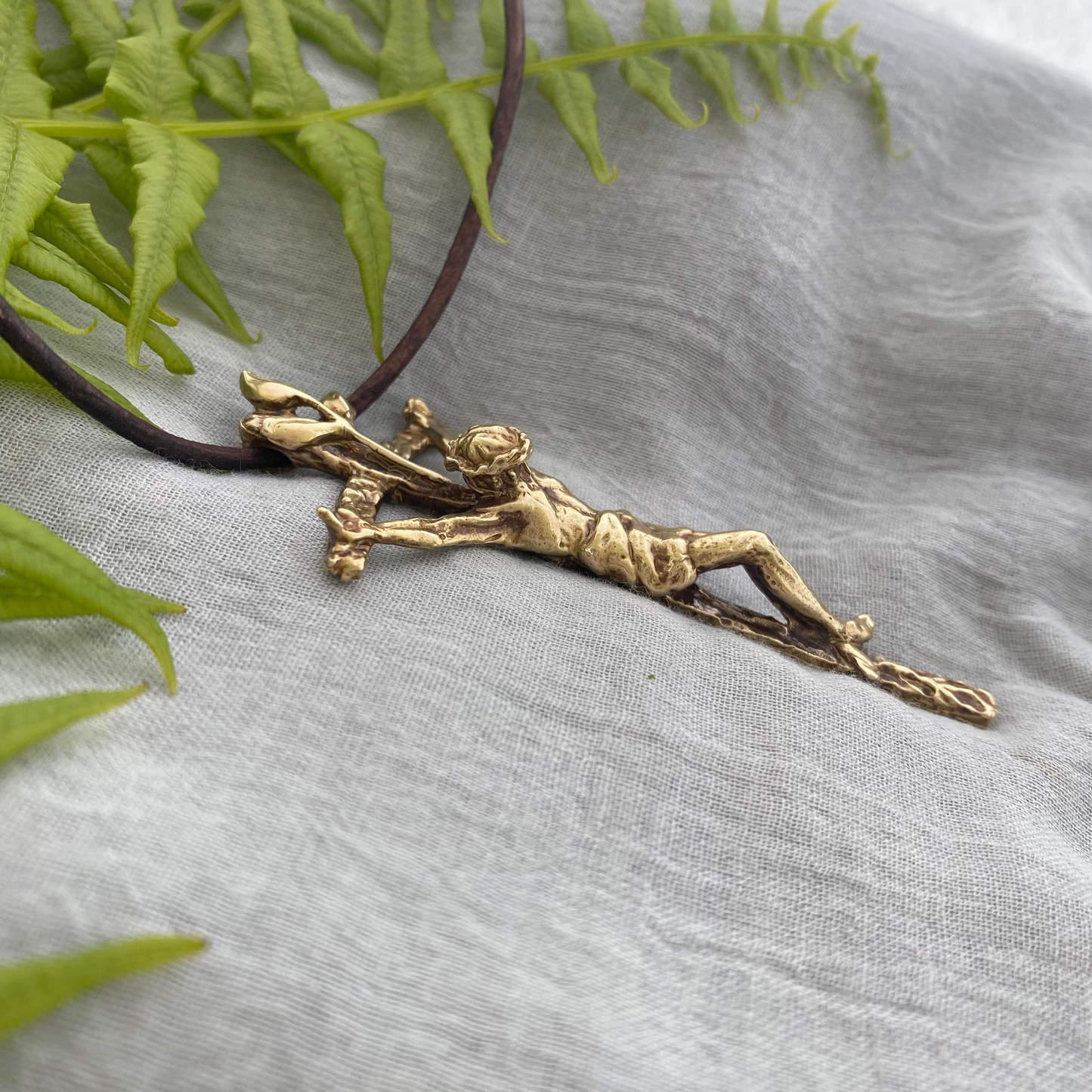 Large brass crucifix necklace; brown leather cord; realistic hand carved corpus; Jesus' suffering, death; leaves symbolizing new life