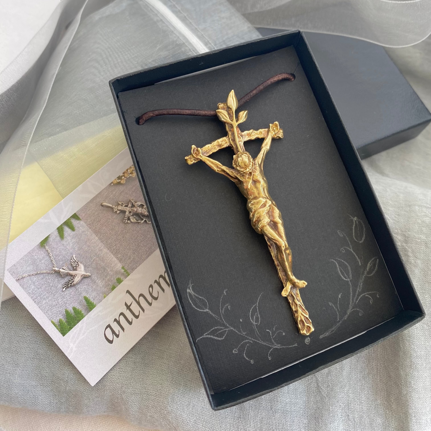 Large brass crucifix necklace; brown leather cord; realistic hand carved corpus; Jesus' suffering, death; leaves symbolizing new life