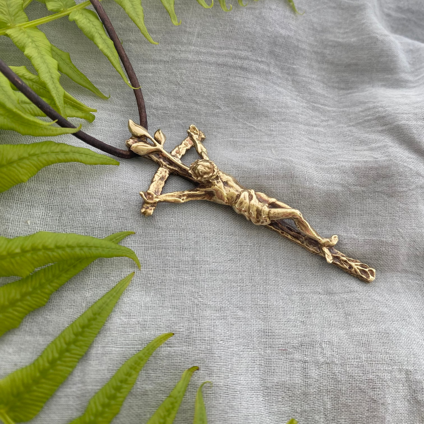 Large brass crucifix necklace; brown leather cord; realistic hand carved corpus; Jesus' suffering, death; leaves symbolizing new life