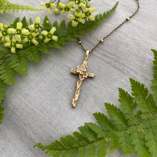 Dainty antiqued brass cross necklace with forget-me-not blossoms and leaves and wood grain texture on antiqued brass satellite cable chain