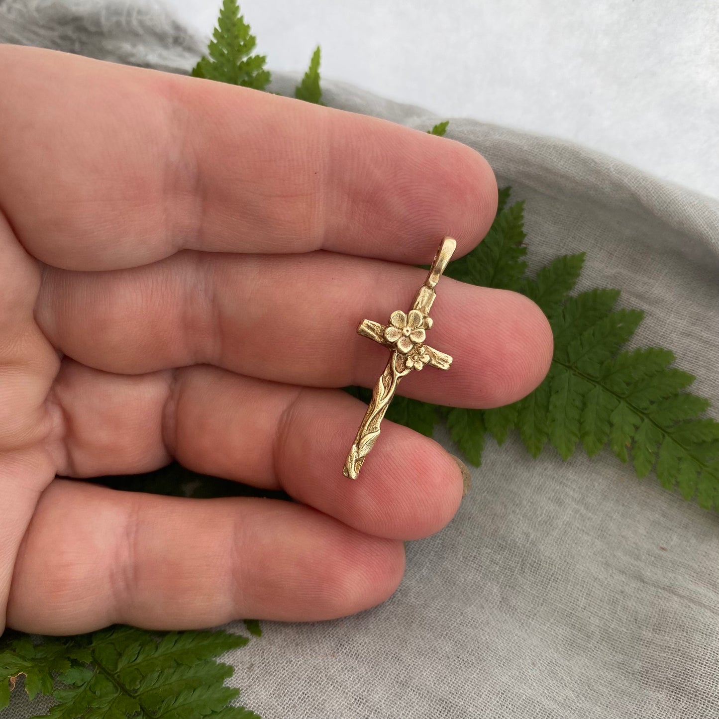 Dainty floral cross pendant for a necklace; gold toned brass; forget-me-not blossoms, leaves, wood grain texture; feminine flower; no chain